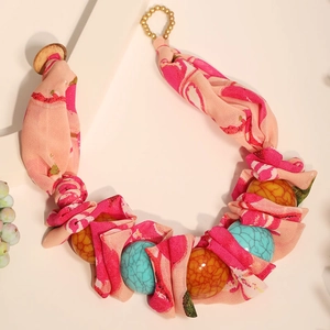 Détail du tissu en mousseline fleurie rose et des perles bleues sur un collier boho