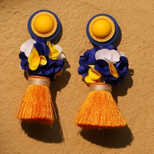 Handmade long tassel earrings with blue and yellow floral accents on yellow wall