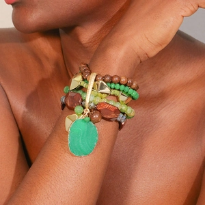 Detail of layered bohemian bead bracelets featuring a green stone pendant and gold metal accents
