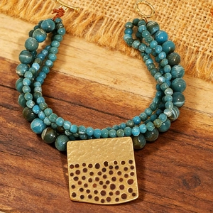 Close-up of bohemian layered beaded bracelet with turquoise stones and gold metal pendant