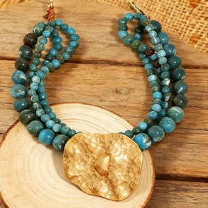 Macro detail of multi-layered blue beaded necklace with hammered gold heart pendant