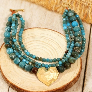 Macro detail of multi-layer beaded necklace with textured gold heart pendant on wood