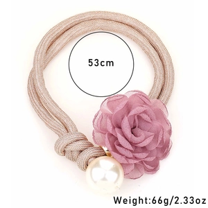 Detail of a pink woven curtain tieback with purple chiffon flower and a large pearl