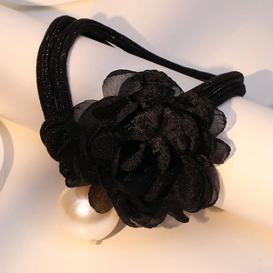 Macro shot of large black chiffon flower and glossy white pearl on woven necklace band