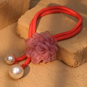 Macro view of a red braided rope necklace with a large pink fabric flower and white pearls