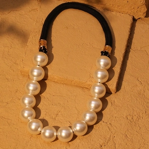 Elegant large white pearl necklace with black rope cord shown on a rustic stone background