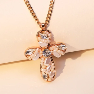 Collana con pendente a croce dorata con perle bianche e cristalli su sfondo beige caldo