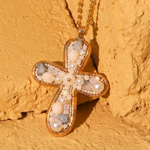 Gold cross necklace with faux pearls and crystals on a warm textured stone background