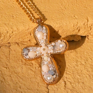 Golden cross necklace with faux pearls and crystals on a rustic textured background