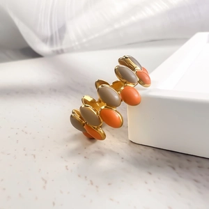 Detail of gold spiral ring with grey and coral orange enamel on white textured background