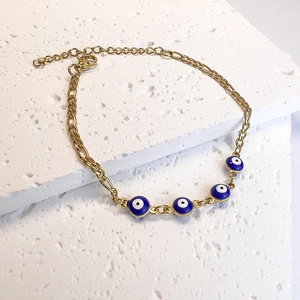 Detailed macro of gold-plated Evil Eye chain bracelet with blue enamel beads on stone