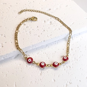 Detail view of gold Figaro chain bracelet featuring red Evil Eye charms on stone