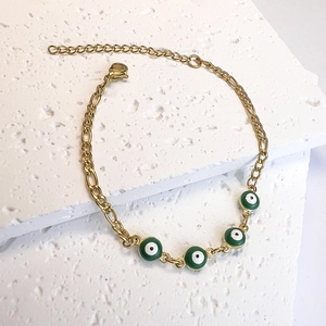 Detail of gold chain bracelet featuring green evil eye charms on a textured stone