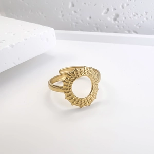 Detail of gold sunburst hollow ring with granular texture on minimalist stone background