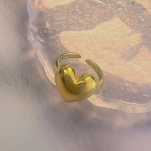 Close-up of golden puffy heart ring on glass tray with sunset lighting effect