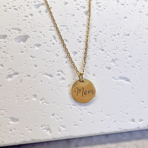 Polished gold MOM necklace with a hollow round pendant on a textured stone background