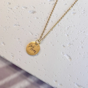 Macro view of gold MOM pendant necklace on textured stone background with detailed engraving