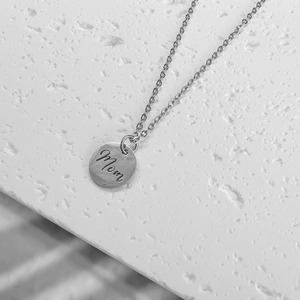 Polished silver stainless steel round pendant necklace with MOM engraving on white surface