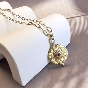 Gros plan du pendentif rond doré texturé avec zircon rouge sur support blanc