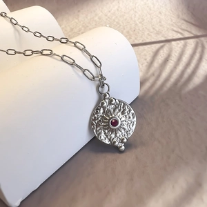 Détail d'un collier vintage en argent avec texture soleil et pendentif zircon rouge
