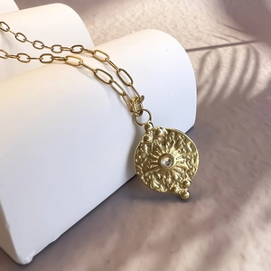 Gros plan d'un collier médaillon doré motif soleil serti d'un zircon cubique