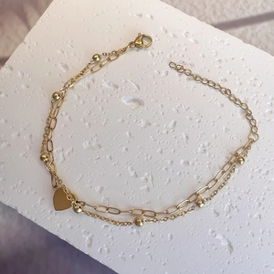 Detail of double-layer gold heart bracelet on a white stone with lobster clasp closure