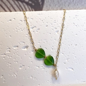 Détail du collier en Y doré avec deux cœurs verts et une perle baroque suspendue