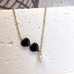 Détail du collier en Y doré avec des breloques cœur noires et une perle baroque