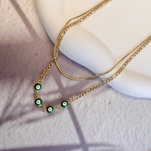 Detail of double-layered 18K gold Figaro chain featuring green evil eye enamel charms