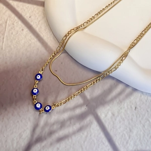 Close-up of double-layer evil eye necklace with gold Figaro chain on a white display