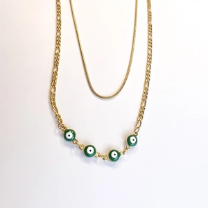 Detail of gold double-layer necklace with green evil eye charms and figaro chain