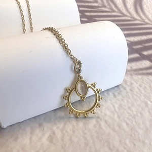Golden sunburst pendant necklace with pink cat eye stone on a minimalist white stand