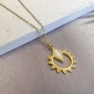 Macro detail of sunburst pendant with white oval gemstone on a golden cross chain