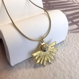 Close-up of a gold fan-shaped necklace with natural stone on a white geometric stand