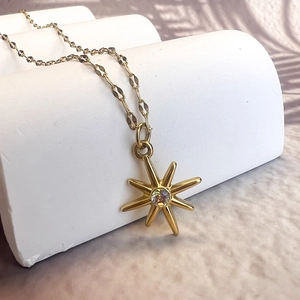Detail of gold stainless steel necklace with starburst pendant and sparkling gemstone