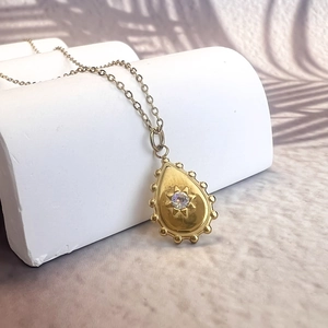 Detail of drop-shaped gold starburst pendant with crystal on geometric pedestal