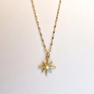 Close-up of golden stainless steel necklace with starburst zircon pendant and faceted chain