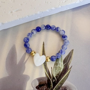Dettaglio dell'anello in pietre naturali con ciondolo a cuore bianco e accenti dorati