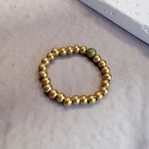 3mm gold beaded stretch ring featuring a green natural stone accent on lilac background