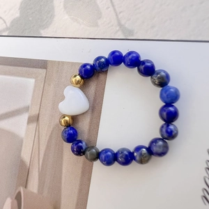 Anello di perle di lapislazzuli con accenti dorati e ciondolo a cuore bianco su rivista