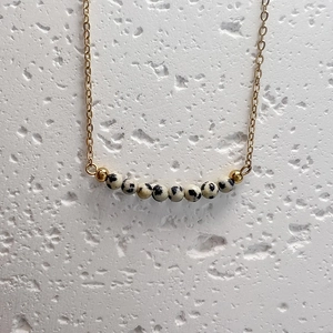 Macro shot of gold chain necklace with natural dalmatian jasper beads on stone surface