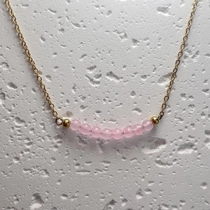Macro view of dainty gold chain necklace featuring small translucent pink quartz beads