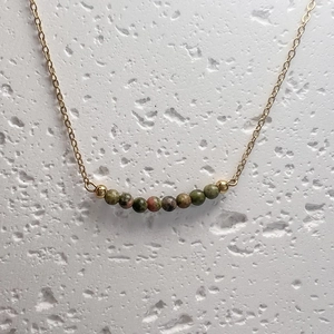 Close-up of Unakite natural stones on a gold chain necklace over a white stone surface