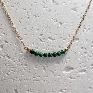 Close-up of nine green malachite beads on a gold chain necklace over stone surface