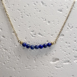 Macro view of gold chain necklace featuring seven blue lapis lazuli beads on stone surface