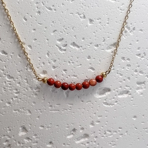 Detail of delicate gold chain necklace featuring red natural stone beads on a stone backdrop