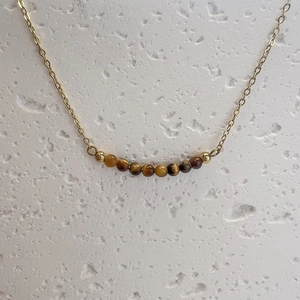 Macro shot of tiger eye beads on a thin gold chain against a white stone background