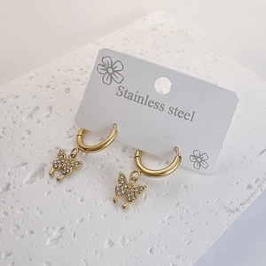 Boucles d'oreilles créoles papillon dorées avec cristaux blancs sur fond de pierre blanche