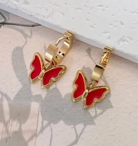 Detail of gold butterfly hoop earrings featuring glossy red enamel and metallic texture