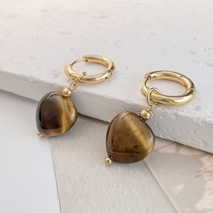 Detail of heart-shaped tiger eye stone earrings with gold hoops on marble surface